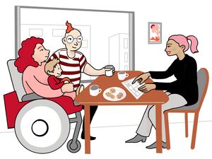 Drei Personen sitzen an einem Tisch. Eine Frau sitzt im Rollstuhl und hält ein kleines Kind auf dem Schoß. Neben ihr sitzt ein Mann. Ihnen gegenüber sitzt eine Frau. Sie zeigt auf ein Papier. Auf dem Tisch stehen Tassen und ein Teller mit Keksen.